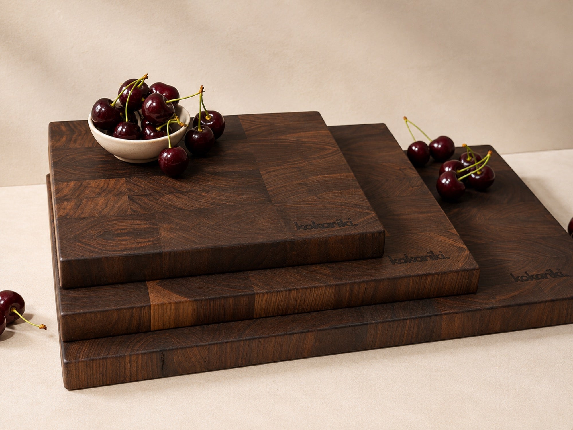 Black walnut end-grain cutting boards stacked in warm morning light, a bowl of cherries resting on top