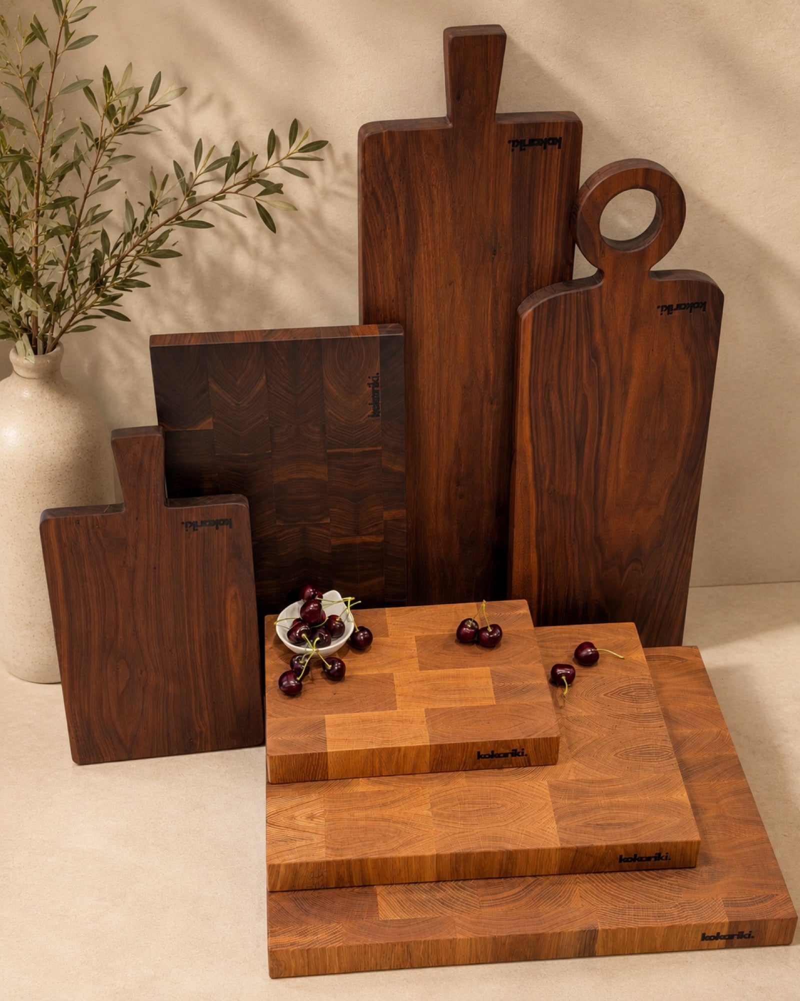 The Kokariki family of boards against a warm plaster wall, olive branches casting shadows